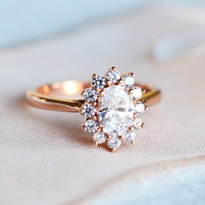 May include: A rose gold engagement ring with an oval-shaped center stone surrounded by a halo of smaller diamonds.