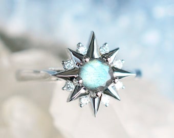 May include: A silver ring with a starburst design featuring a blue-green labradorite gemstone surrounded by clear round stones.