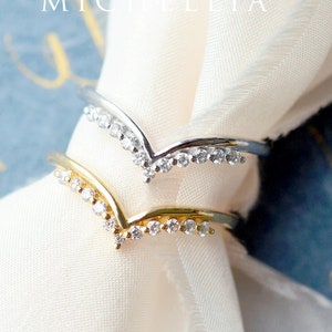 May include: Two delicate rings with a V-shaped design, each adorned with a row of sparkling clear stones.
