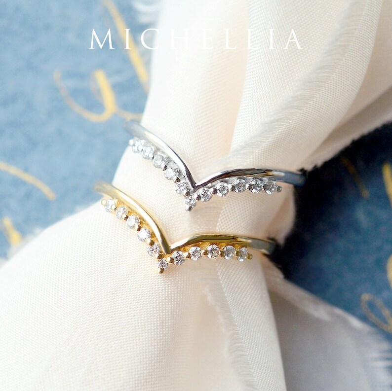 May include: Two delicate rings with a V-shaped design, each adorned with a row of sparkling clear stones.