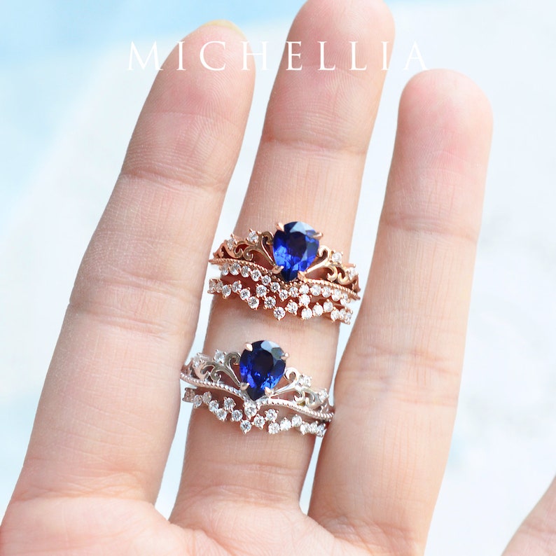Pu&ograve; includere: Due anelli con una pietra centrale di zaffiro blu e un design a corona. L'anello superiore &egrave; in oro rosa con una fascia di piccoli diamanti. L'anello inferiore &egrave; in argento con una fascia di piccoli diamanti.
