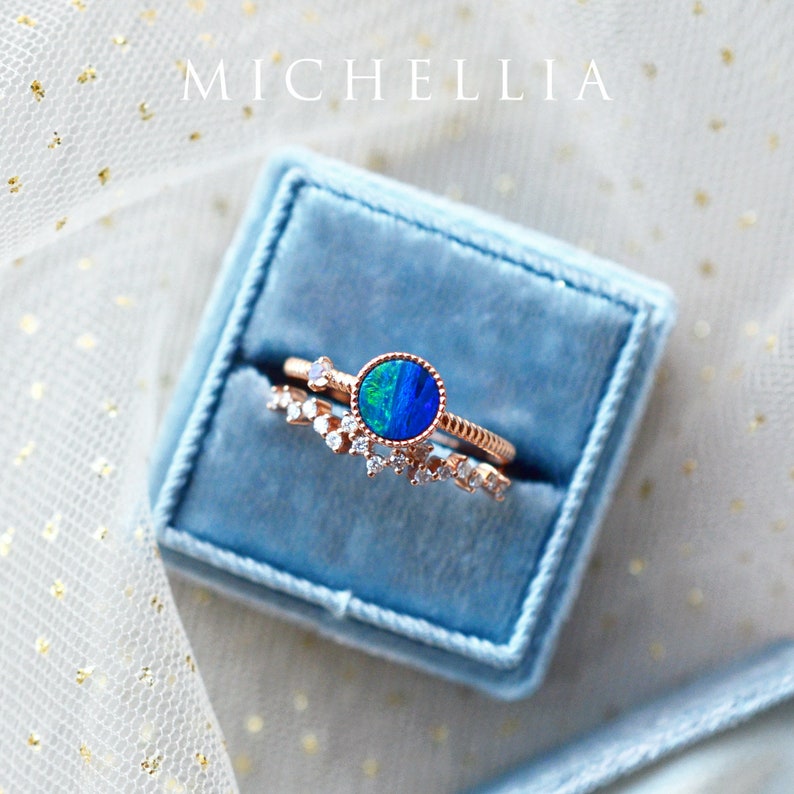 Pu&ograve; includere: Un set di due anelli in oro con una pietra preziosa di opale blu e piccoli diamanti. Gli anelli sono in una scatola di anello in velluto blu.