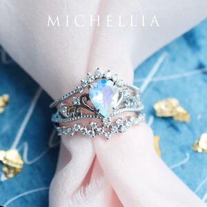 Pu&ograve; includere: Un anello d'argento con una pietra di luna a forma di pera incastonata in un design delicato e ornato. L'anello &egrave; circondato da diamanti pi&ugrave; piccoli e ha un aspetto delicato e femminile.