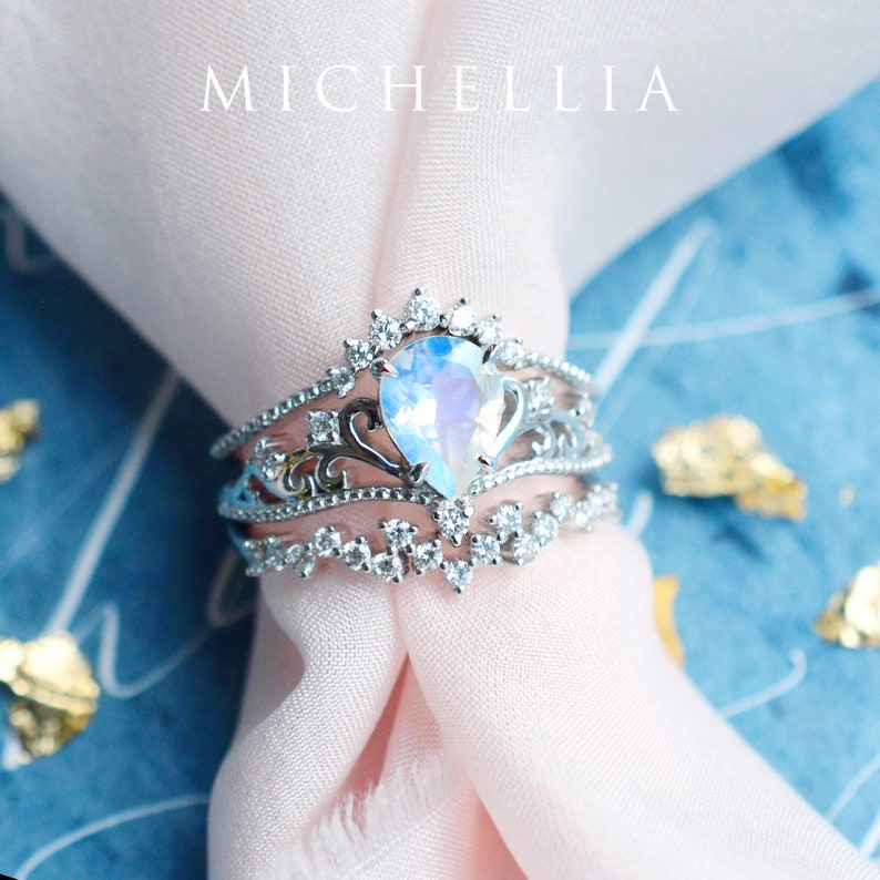 Pu&ograve; includere: Un anello d'argento con una pietra di luna a forma di pera incastonata in un design delicato e ornato. L'anello &egrave; circondato da diamanti pi&ugrave; piccoli e ha un aspetto delicato e femminile.