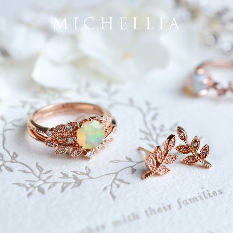 Op de afbeelding: Een set delicate ros&eacute;gouden sieraden met een ring met een witte opaal-edelsteen en bladeren accenten, en een paar bijpassende blad oorbel studs.