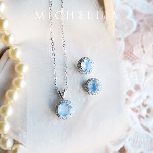 Pu&ograve; includere: Un set di collana e orecchini in argento con un ciondolo in pietra di luna blu e orecchini abbinati. Le pietre sono circondate da un alone di pietre chiare pi&ugrave; piccole.