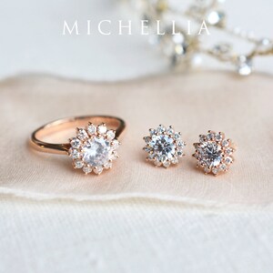 May include: A set of rose gold jewelry featuring a ring and a pair of earrings. The ring and earrings have a delicate, floral design with a central round stone surrounded by smaller stones.