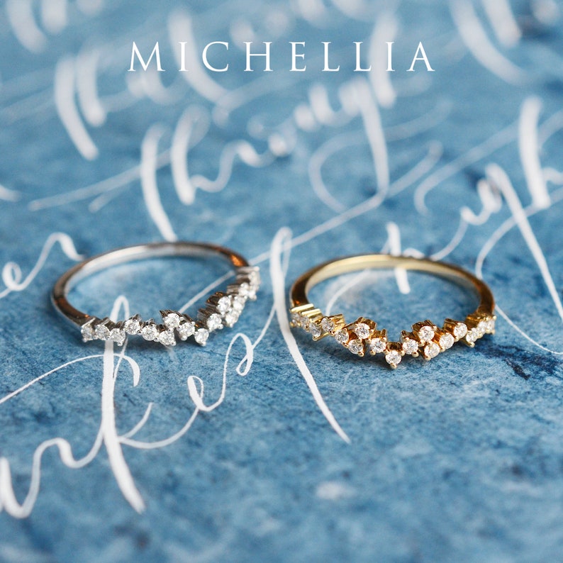 Pu&ograve; includere: Due anelli delicati con un designo di diamanti scintillanti. Gli anelli sono su uno sfondo blu con scrittura bianca in corsivo. La parola "MICHELLIA" &egrave; scritta in bianco nella parte superiore dell'immagine.