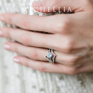 May include: A silver ring set with a large oval moonstone surrounded by smaller diamonds. The ring is worn on the ring finger of a hand.