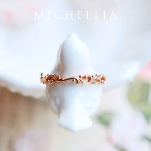 K&ouml;nnte beinhalten: Ein zarter Ring aus Ros&eacute;gold mit floralem Design. Der Ring befindet sich auf einem wei&szlig;en, vogelartigen Pr&auml;sentationsst&auml;nder.