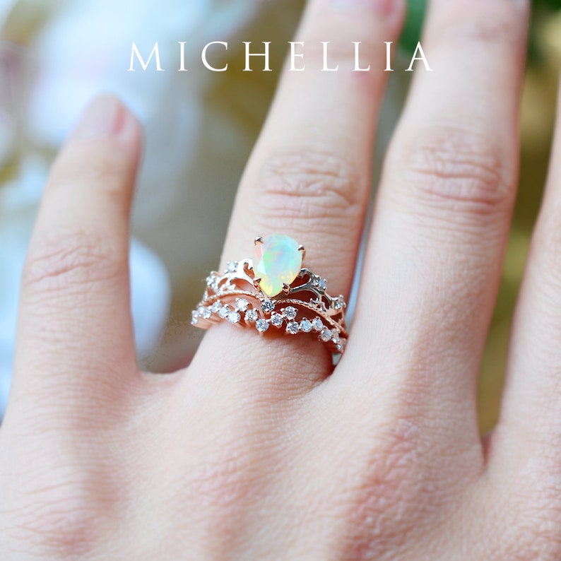 Pu&ograve; includere: Un delicato anello in oro rosa con un'opale a forma di pera e una fascia di diamanti pi&ugrave; piccoli. L'anello &egrave; su un dito.