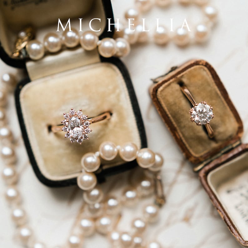 May include: Two engagement rings in velvet boxes. The ring on the left has a large oval-shaped diamond surrounded by smaller diamonds. The ring on the right has a round diamond surrounded by smaller diamonds. Both rings are set in rose gold.
