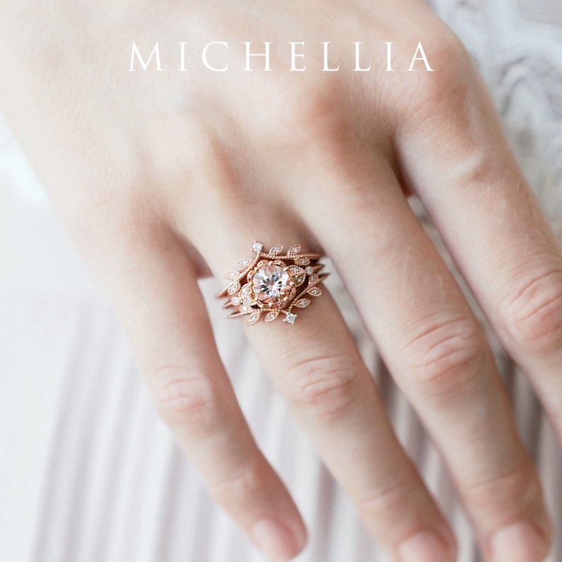 May include: Rose gold engagement ring with a delicate floral design and a round center stone. The ring is set with small diamonds and has a leafy pattern.