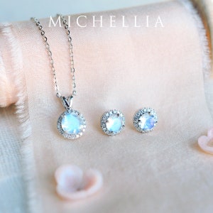 Pu&ograve; includere: Una collana d'argento con un ciondolo rotondo in pietra di luna circondato da un'aureola di diamanti pi&ugrave; piccoli. Sono anche raffigurati orecchini abbinati con pietre rotonde in pietra di luna e anelli di diamanti.