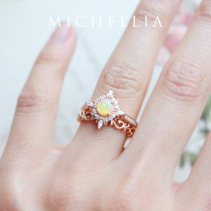 K&ouml;nnte beinhalten: Ein Ring aus Ros&eacute;gold, besetzt mit einem gro&szlig;en, ovalen Opal, der von kleineren, runden Diamanten umgeben ist. Der Ring hat ein zartes, florales Design.