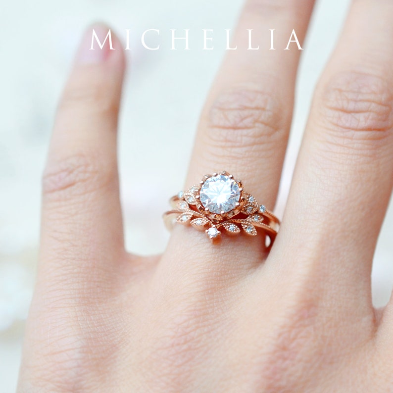 May include: A rose gold engagement ring with a large round center stone and a delicate floral design. The ring is set with smaller diamonds around the center stone and on the band.