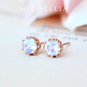 May include: A pair of rose gold earrings with a round, iridescent gemstone set in a crown-like design. The earrings are on a white background.