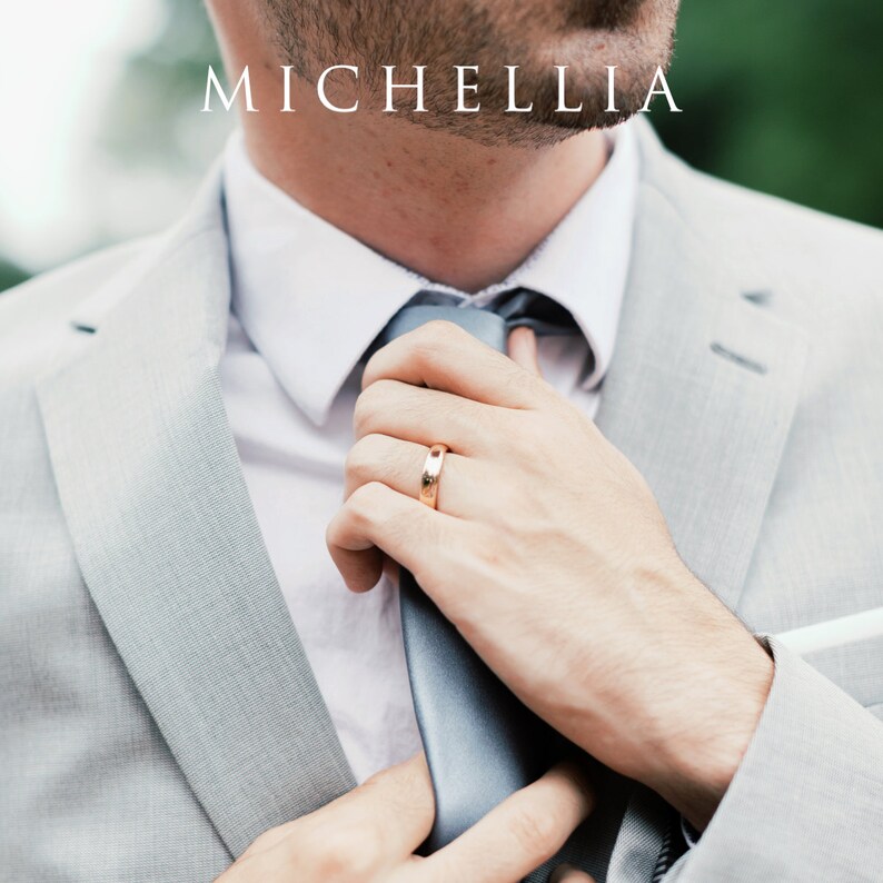 May include: A person in a light gray suit and white shirt adjusting a gray tie. A gold wedding band is visible on the ring finger. The word "MICHELLIA" is printed in white at the top of the image.