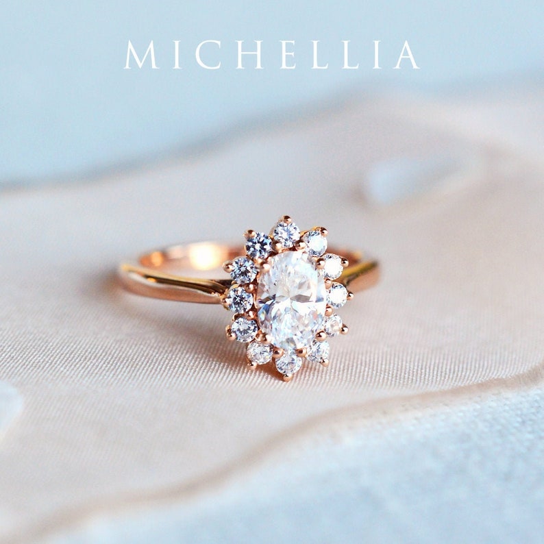 May include: A rose gold engagement ring with an oval-shaped center stone surrounded by a halo of smaller diamonds.