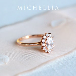 May include: A rose gold engagement ring with a large oval-shaped center stone surrounded by a halo of smaller diamonds.