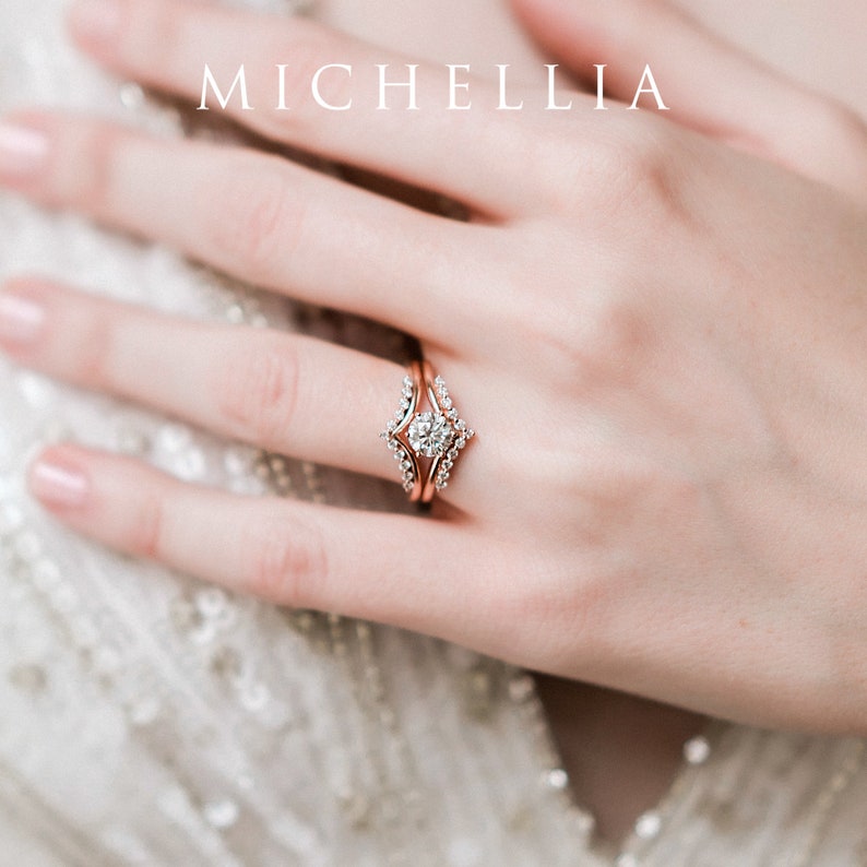 May include: A rose gold engagement ring set with a round center stone and a delicate band. The ring is set with smaller diamonds on the band and the center stone is surrounded by a halo of smaller diamonds.
