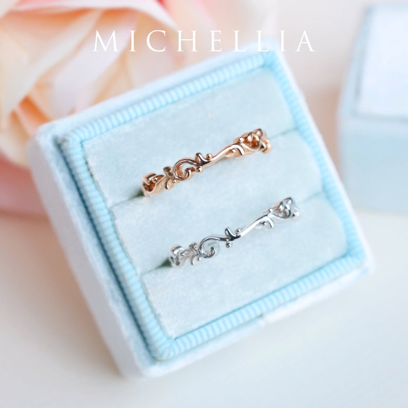 K&ouml;nnte beinhalten: Zwei zarte Ringe mit filigranen Blumenmustern, einer in Ros&eacute;gold und einer in Silber, pr&auml;sentiert in einer hellblauen Samt-Ringbox. Die Box ist mit "MICHELLIA" beschriftet.