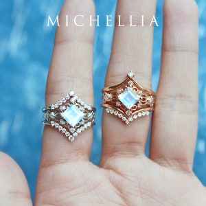 May include: Two silver and rose gold rings with a square moonstone center stone and a delicate filigree design. The rings are set with small diamonds and are worn on a finger.