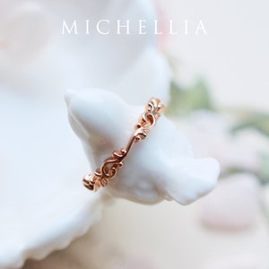 K&ouml;nnte beinhalten: Ein zarter Ros&eacute;goldring mit einem filigranen, komplizierten Design. Der Ring besteht aus einem d&uuml;nnen Band mit einem sich wiederholenden Muster aus Wirbeln und Kurven.