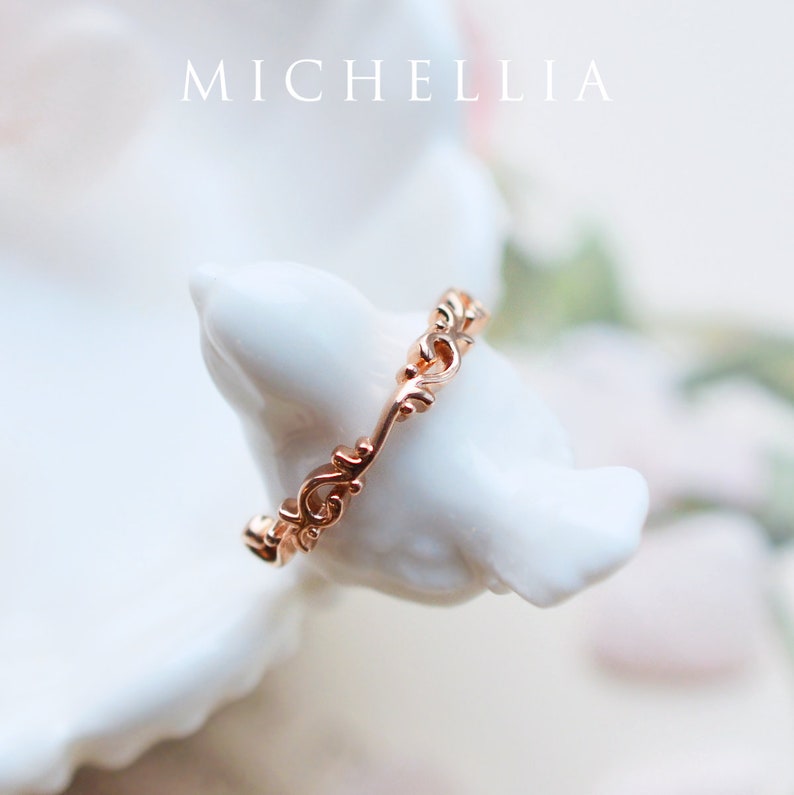 K&ouml;nnte beinhalten: Ein zarter Ros&eacute;goldring mit einem filigranen, komplizierten Design. Der Ring besteht aus einem d&uuml;nnen Band mit einem sich wiederholenden Muster aus Wirbeln und Kurven.