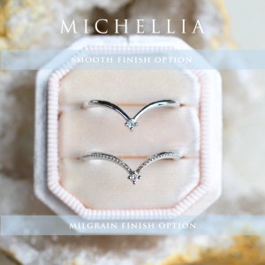 May include: Two silver V-shaped rings with a single diamond in the center of each. The top ring has a smooth finish, while the bottom ring has a milgrain finish. The rings are displayed in a white velvet ring box.  "MICHELLIA" and "SMOOTH FINISH OPTION" and "MILGRAIN FINISH OPTION" are written in black text on the image.