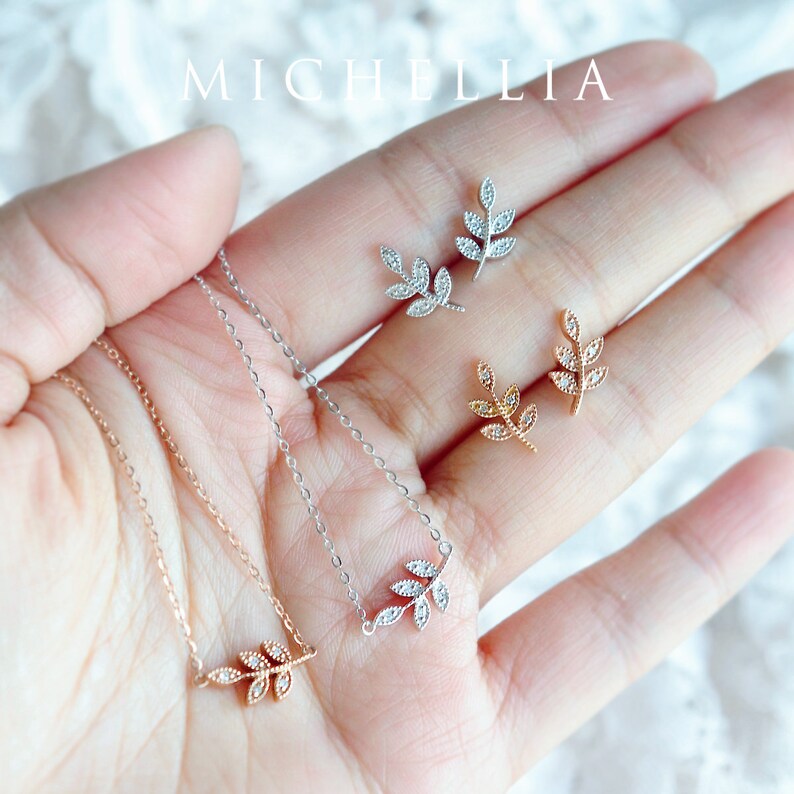 Op de afbeelding: Een set van drie delicate bladvormige kettingen en oorbellen. De sieraden zijn gemaakt van zilver, goud en ros&eacute;goud, en elk stuk is versierd met glinsterende zirkonia-stenen.