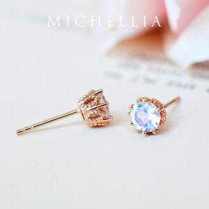 May include: A pair of rose gold earrings with a round, iridescent gemstone set in a delicate crown-shaped setting. The earrings have a post back.