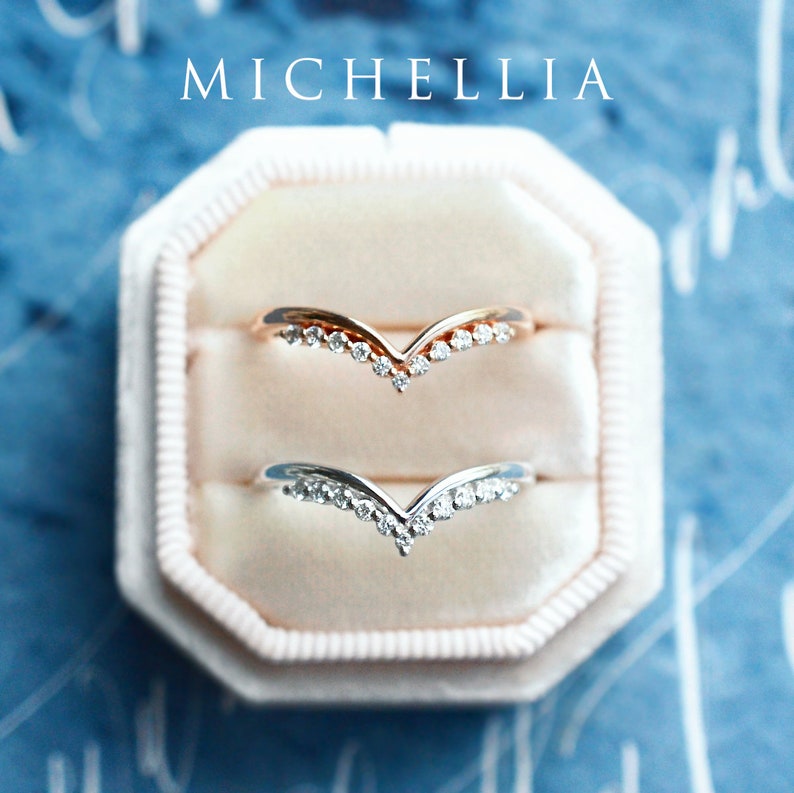 May include: Two delicate V-shaped rings with a row of small diamonds set in a gold and silver band. The rings are displayed in a white ring box.
