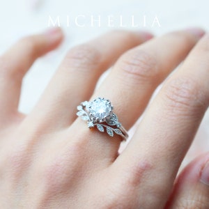 May include: A silver ring set with a large, round, clear gemstone surrounded by smaller gemstones. The ring is set with a delicate, leafy design.