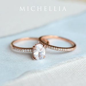 May include: A set of two rose gold engagement rings with a large oval-shaped center stone and a smaller band with pave diamonds.