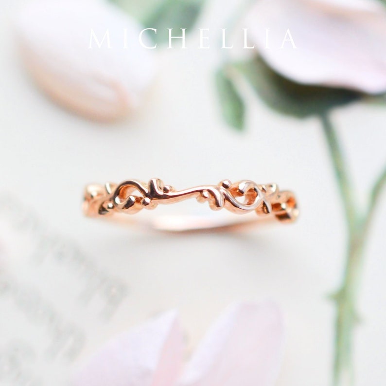 K&ouml;nnte beinhalten: Ein zarter Ring aus Ros&eacute;gold mit einem filigranen, kunstvollen Blumenmuster. Der Ring besteht aus einem d&uuml;nnen Band mit einem zarten, wirbelnden Muster.