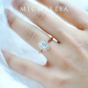 May include: A rose gold engagement ring with an oval-shaped center stone surrounded by a halo of smaller stones.