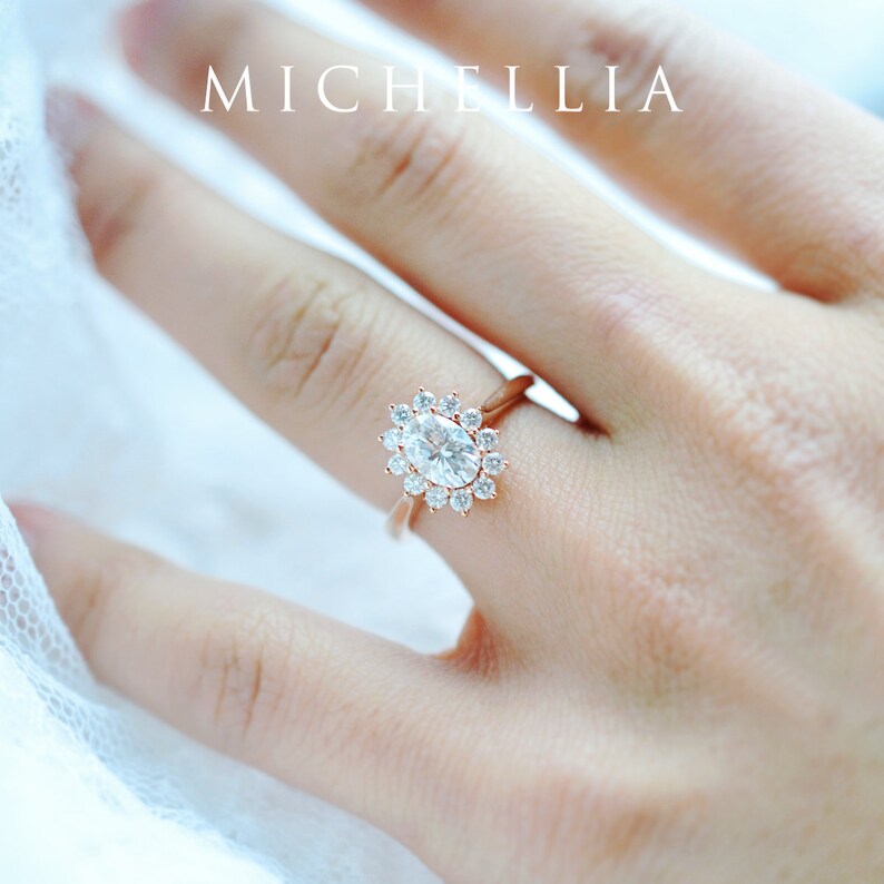 May include: A rose gold engagement ring with an oval-shaped center stone surrounded by a halo of smaller stones.