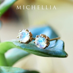 May include: A pair of gold stud earrings with iridescent moonstone gemstones. The earrings are set in a delicate crown design.