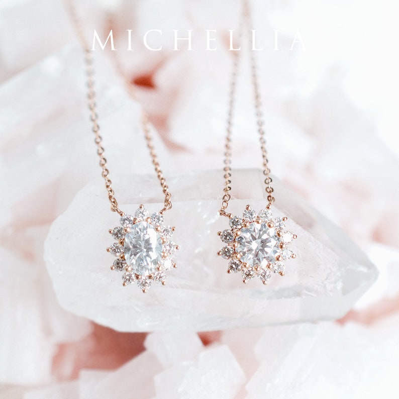 May include: Two delicate gold necklaces with a round diamond pendant surrounded by smaller diamonds. The necklaces are displayed on a white crystal surface.