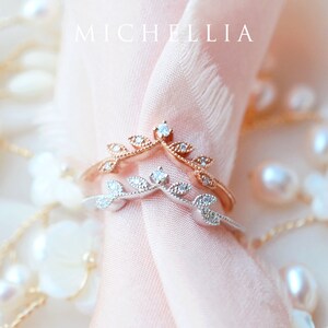 May include: Two delicate rings with a leaf and diamond design. The rings are stacked on top of each other, with the top ring being rose gold and the bottom ring being silver.