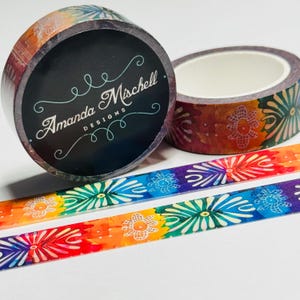 May include: Decorative washi tape rolls with a floral design in rainbow colors. One roll features the text "Amanda Mischell DESIGNS" on a black background. Two strips of tape are unrolled, showing the colorful floral pattern.