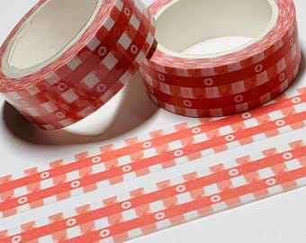 Puede incluir: Dos rollos de cinta adhesiva decorativa con un patrón de cuadros rojos y blancos. La cinta tiene un patrón repetitivo de cuadrados rojos y cruces blancas. Debajo se ven tiras de la misma cinta.