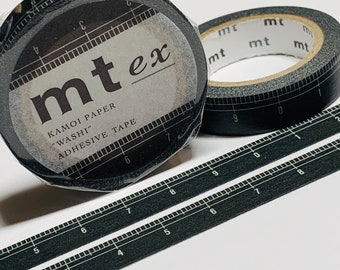 Puede incluir: Dos rollos de cinta washi negra con un diseño de regla. La cinta está etiquetada como "mt ex" y "Kamoi Paper "Washi" Adhesive Tape".