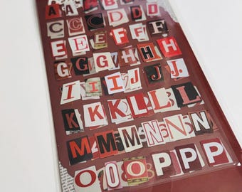 Puede incluir: Una hoja de pegatinas del alfabeto con una estética de collage. Las letras están recortadas de varias fuentes, con colores rojo y negro. La palabra "Relater" está impresa en la parte superior. Las pegatinas están en un paquete de plástico transparente.