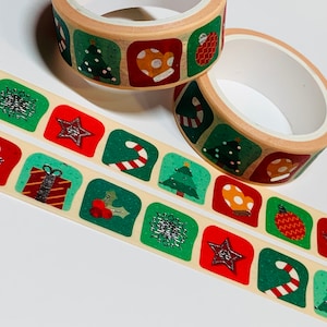 May include: Two rolls of washi tape with a Christmas theme. The tape features a variety of festive designs, including snowflakes, candy canes, Christmas trees, and mittens. The tape is beige with green and red accents.