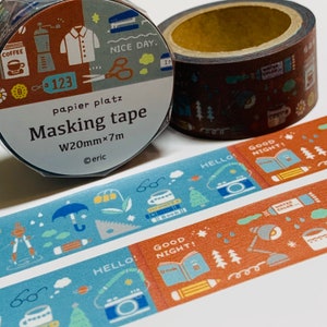 May include: Two rolls of washi tape with different designs. The first roll has a blue and brown background with illustrations of coffee, a shirt, scissors, and a stapler. The second roll has a brown background with illustrations of a cup of coffee, a book, a pencil, and a lamp. The text on the first roll says "papier platz Masking tape W20mm x 7m @eric". The text on the second roll says "HELLO! GOOD NIGHT! WATER COLOR!"