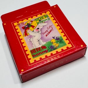 May include: A red box with a white bunny wearing a yellow hat and holding a purple flower. The box has the text "Happy Easter, MOMMY!" and "班尼兔 bunny" on it.