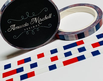 May include: Washi tape rolls with a red, white, and blue plaid pattern. The rolls are next to strips of tape with alternating red and blue squares. The black label on the roll reads "Amanda Mischell Designs."