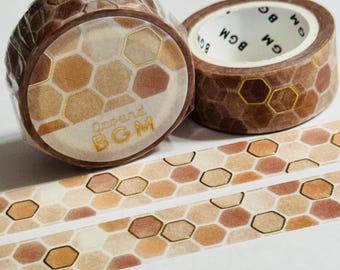 May include: Two rolls of decorative washi tape with a honeycomb pattern in shades of brown, beige, and gold. The tape is labeled "Ground BGM" in gold lettering. A strip of the tape is unrolled, showing the repeating pattern.